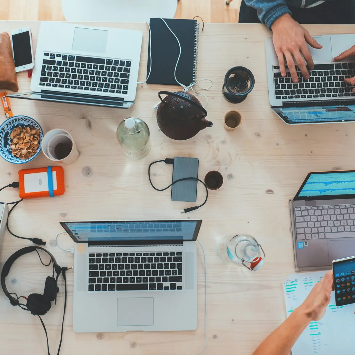 A work table seen from above with several laptops, notebooks, and coffee